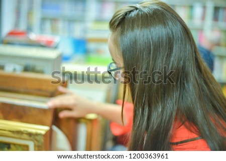 woman in antique shop is selecting among old vintage pictures