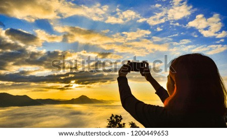 Female tourists are taking pictures of the cloud-covered peaks during the sunrise.