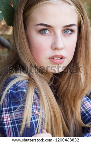 A portrait of a lovely, natural blonde-haired, blue-eyed, teenage girl in a checkered shirt Royalty-Free Stock Photo #1200468832