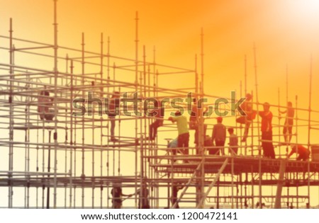 Blurred photo of construction workers working on scaffolding and evening sky