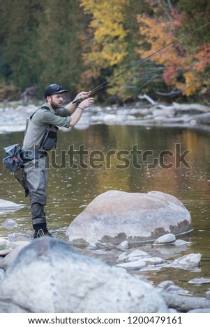 A man fly fishing in the fall in a river