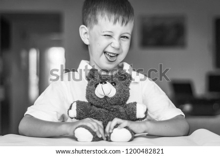 Funny and naughty Caucasian child with a toy teddy bear. Kid showing tongue. Happy childhood concept. Black and white image.
