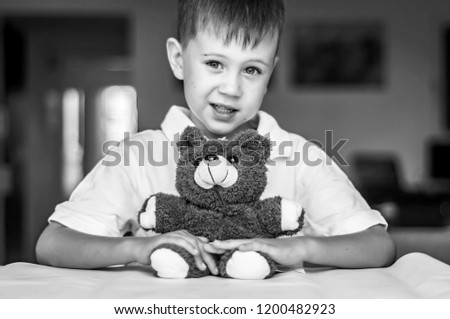 Funny and naughty Caucasian child with a toy teddy bear. Happy childhood concept. Black and white image.
