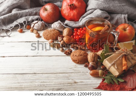 Autumn composition of a cup of warming tea, autumn leaves, fruits and spices on a white wooden table
