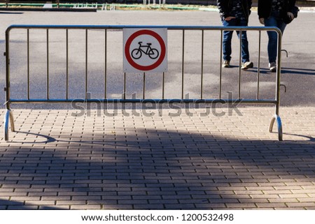 Two pedestrians are walking behind a fence and a sign of the prohibition of Cycling