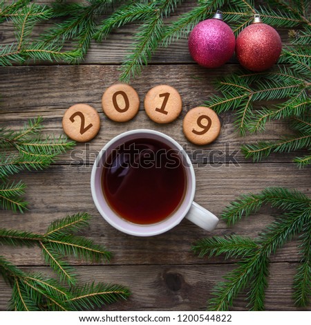 New Year picture with Christmas tree branches and the number 2019 on round cookies with a cup of hot tea on a wooden background
