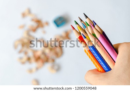 Coloured pencils in hand against blurred shavings on white background.