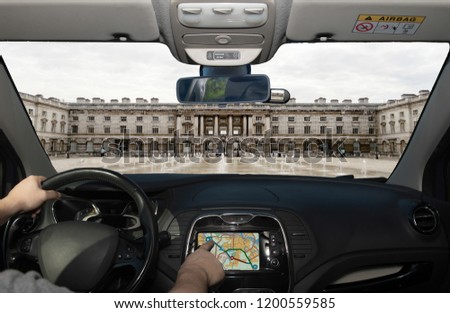 Driving a car while using the touch screen of a GPS navigation system towards Somerset House, Victorian building in the Strand district of London, UK