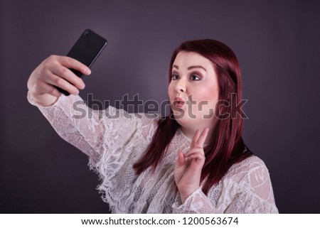 Young college aged woman holding cell phone taking a selfie puckered lips giving peace sign