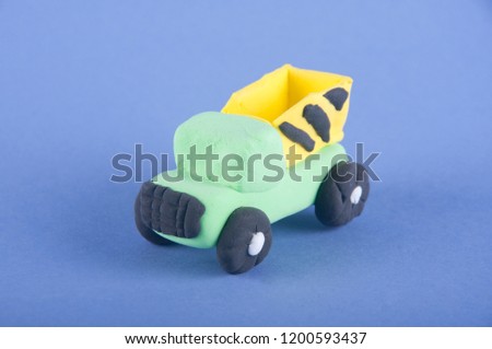 Toy transport. Green, yellow dump truck made of playing clay staying on purple background