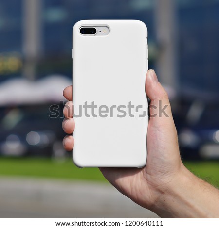 Smart phone on a blurry city background. in a white plastic case back view. Smart phone in man's hand. Template of phone case, iPhone 8 plus case mock up