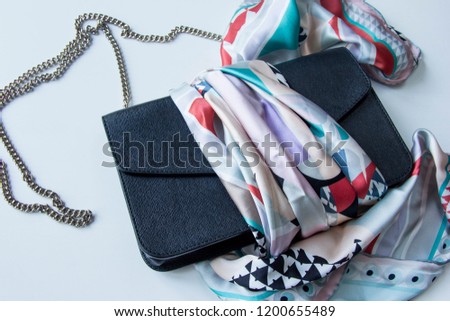High fashion. Stylish lady's handbag of a black textured leather with chain at white background, wrapped in a luxury scarf