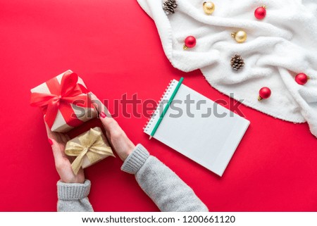Female hands, girl holds a gifts, white Notepad, red table with gift boxes for Christmas and New year, background with copy space, for advertisement, top view