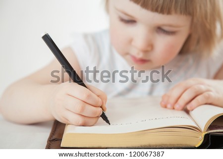 Attentive little girl writing letters with a pen; white background