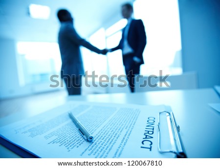 Image of business contract on background of two employees handshaking