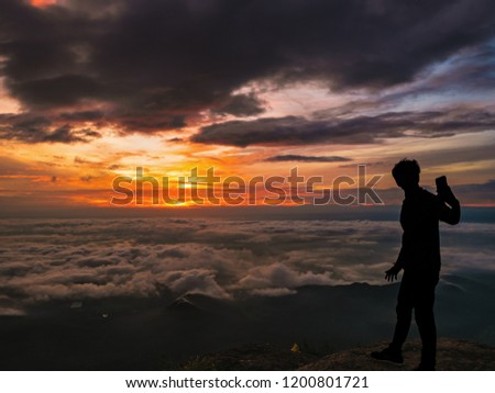 Silhouette People Take a Selfie on the cliff with beautiful sunrise sky on Khao Luang mountain in Ramkhamhaeng National Park,Sukhothai province Thailand