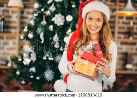 Young woman standing and holding gifts in front of Christmas tree. Christmas holidays concept.