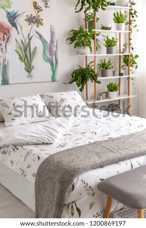 White and green organic linen and gray wool blanket on a bed in a bright bedroom interior full of plants. Real photo.