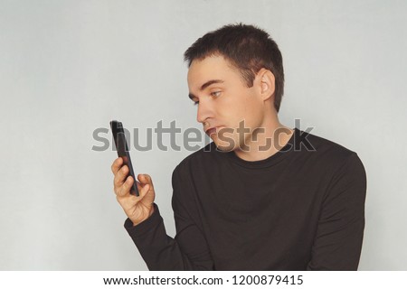 a young guy looks at the screen of a black smartphone with a dismissive emotion on his face. uninteresting correspondence. boring pastime. picture, photograph, photography, image,