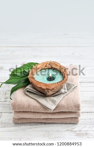 Candle in coconut shell on stack of towels on light background. Spa concept.