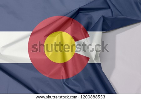 Colorado fabric flag crepe and crease with white space, The states of America, blue white and blue. On top of these stripes sits a circular red "C", filled with a golden disk.