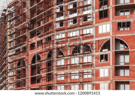 Building construction site with scaffolds. Red high-rise building under construction. Future residential building. Brick residential building with big windows, arches, arcs. Filled full frame picture.