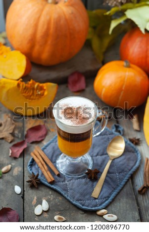 Pumpkin cappuccino on the background of the autumn composition of whole and sliced pumpkins, dried leaves, cinnamon sticks and anise stars. On old wooden boards.