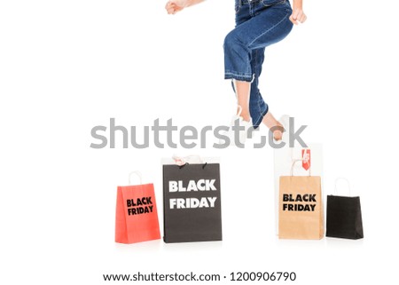 cropped view of girl jumping near shopping bags with black friday sale signs isolated on white