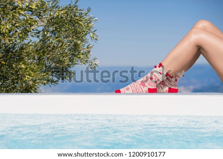 Women's feet in Christmas socks near the pool on the Olive tree and mountain background. Greece
