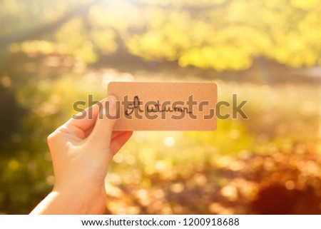 Autumn text on a card.  Girl holding card in a field with a river  in sunny rays.