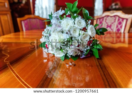 Beautiful wedding rings lie on wooden surface against background of bouquet of flowers. Declaration of love, spring. Wedding card, Valentine's Day greeting. Wedding rings. Wedding day details