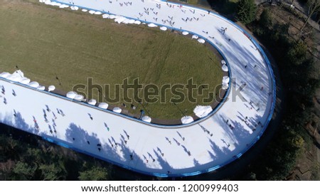 Aerial picture of oval shaped ice rink frozen body of water where people are enjoying winter sports ice-skating this track is mechanically where coolant produces cold temperatures in surface below