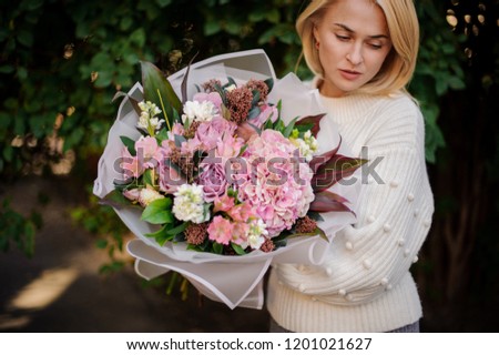 Girl in the white sweather holding in her hands a beautiful bouquet of tender pink autumn flowers in white transparent paper