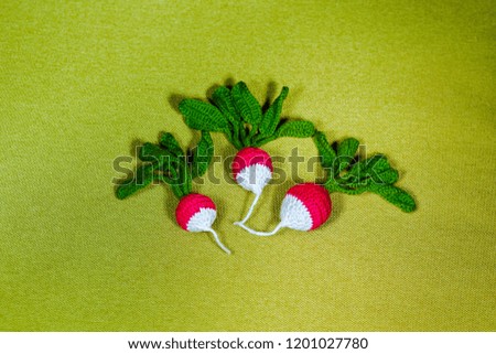 Red and white handmade radish with green bundle on the green background is mage of thread, knitted - soft toy for small children. Symbol of fresh healthy food for vegetarians.