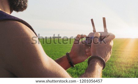 Bearded male model use aerial drone remote control to fly device in sky. Aerial drone flying over sunset green rice fields. Wide banner long format