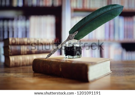 Quill pen and ink well resting on an old book in a library concept for literature, writing, author and history Royalty-Free Stock Photo #1201091191