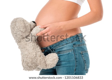 cropped view of pregnant girl holding teddy bear at her tummy isolated on white