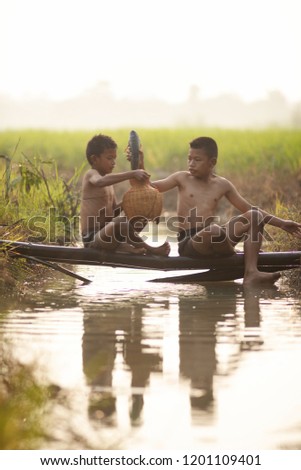Asian children fisherman on the rice field or agricultural paddy field is celebrating the success in fishing and showing a big fish which is getting from the fishing at the river with happiness