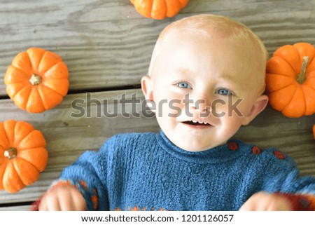 Baby boy on wooden deck with little pumpkins