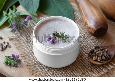 A jar of homemade comfrey ointment with fresh symphytum officinale plant and dried root Royalty-Free Stock Photo #1201196890