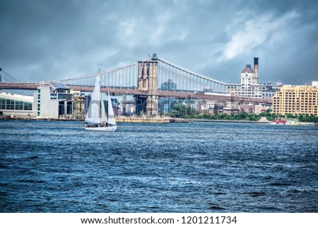 Sailing the Hudson river in a cloudy day next to the Brooklyn Bridge