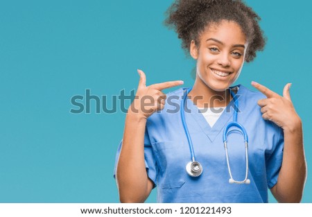 Young afro american doctor woman over isolated background smiling confident showing and pointing with fingers teeth and mouth. Health concept.