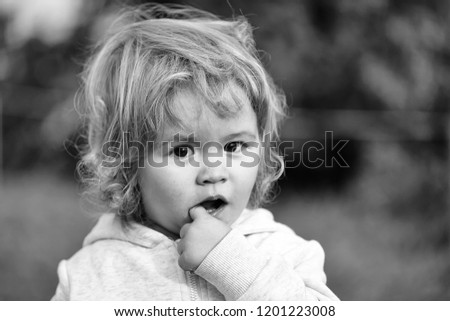 Kid little child baby boy fair-haired blond hazel-eyed smiling wearing grey hooded coat cute portrait with finger in mouth looking at camera on blurred natural background, horizontal picture