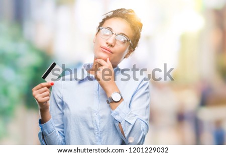 Young african american girl holding credit card over isolated background serious face thinking about question, very confused idea