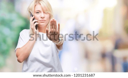 Young beautiful blonde woman calling and talking on smartphone over isolated background with open hand doing stop sign with serious and confident expression, defense gesture
