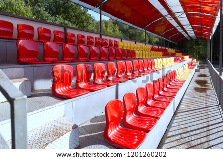 Empty street seats in red and yellow on the podium under a canopy to watch sporting events in the stadium.