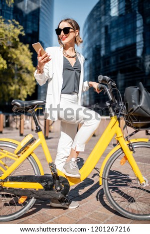Portrait of a stylish business woman in white suit standing with bicycle at the financial district with modern buildings on the background