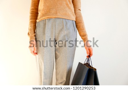 Young slim woman in classic fashionable outfit, brown sweater and loose grey pants, shopping, holding paper bags. White background, copy space, close up. Black friday sale concept.