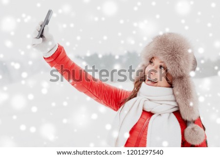 people, technology and leisure concept - happy woman in winter fur hat taking selfie by smartphone outdoors