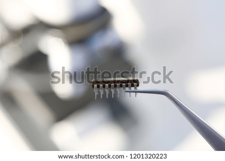 An employee of computer repair service assembly keeps spare part motherboard processor with tweezers for installation using method of soldering technology development